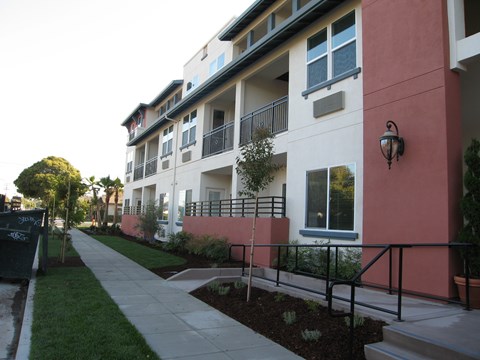 A building with a red and white facade has a balcony and a small garden in front.