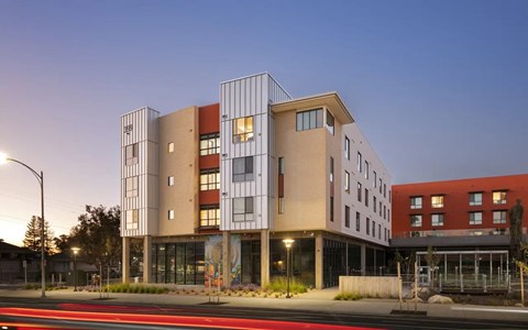 A modern building with a mix of beige and red colors is illuminated by street lights.