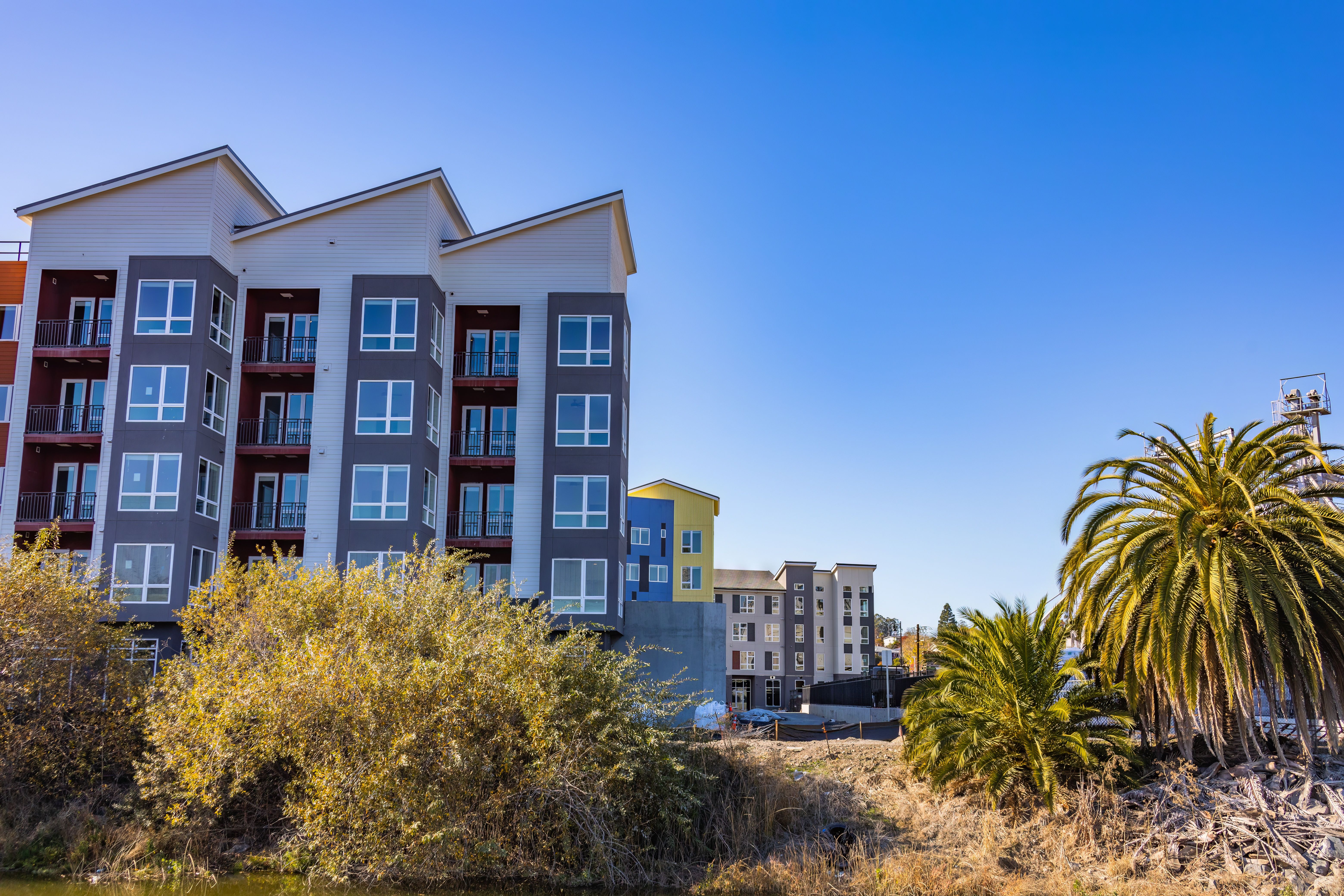 A modern apartment building with a yellow accent building in the background.