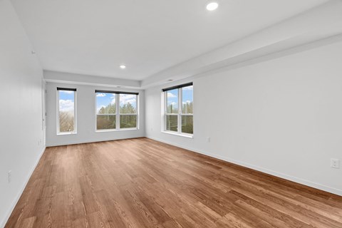 an empty living room with a wood floor and three windows