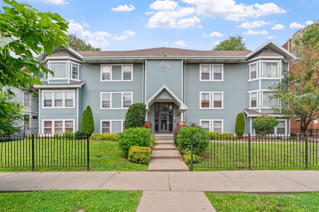 a blue house with a sidewalk and a wrought iron fence