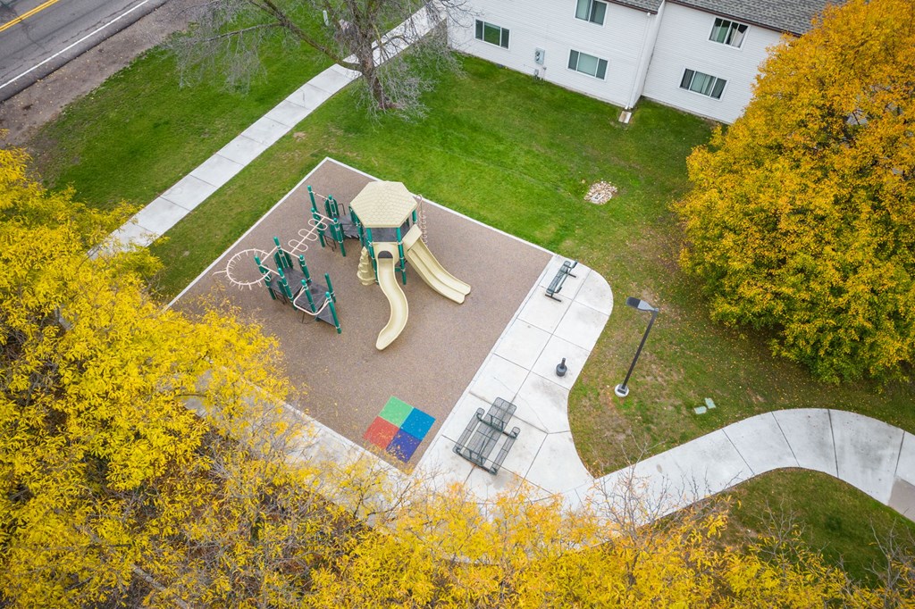A playground with a slide and swings surrounded by trees with yellow leaves.