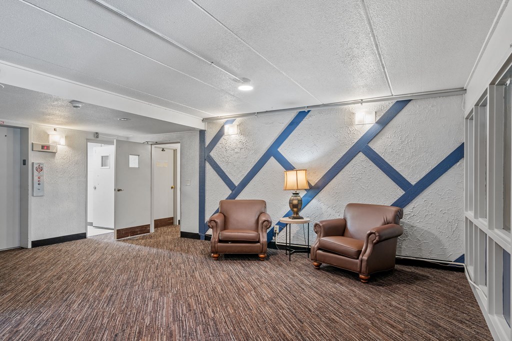 a lobby with two chairs and a table with a lamp