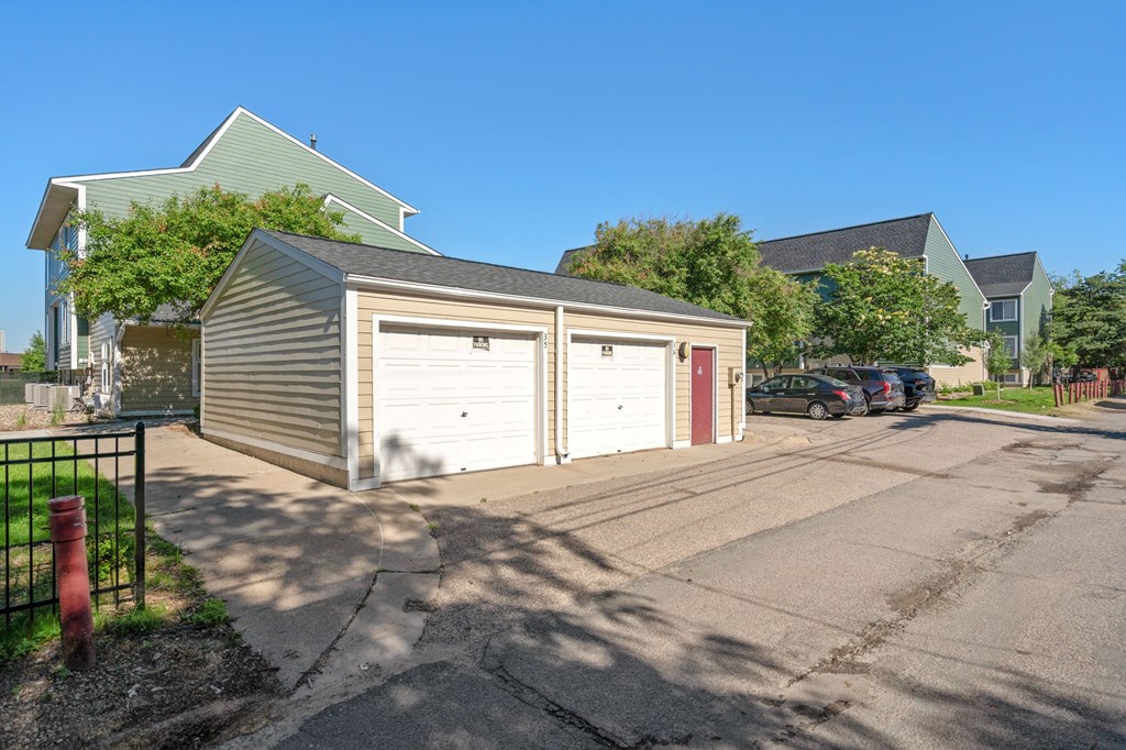 a garage with two white doors and a driveway in front of a house