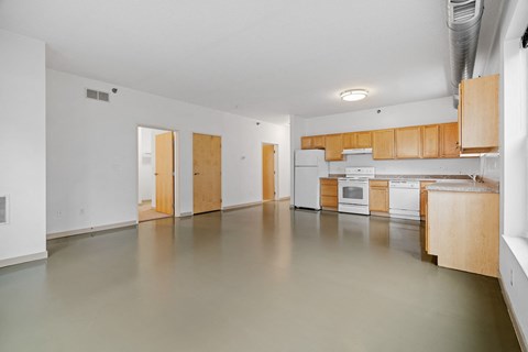 the living room and kitchen of an empty apartment with white appliances and wood cabinets