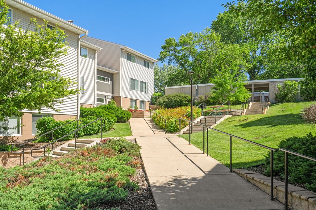 a sidewalk in front of a building with stairs and trees