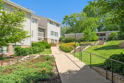 a sidewalk in front of a building with stairs and trees