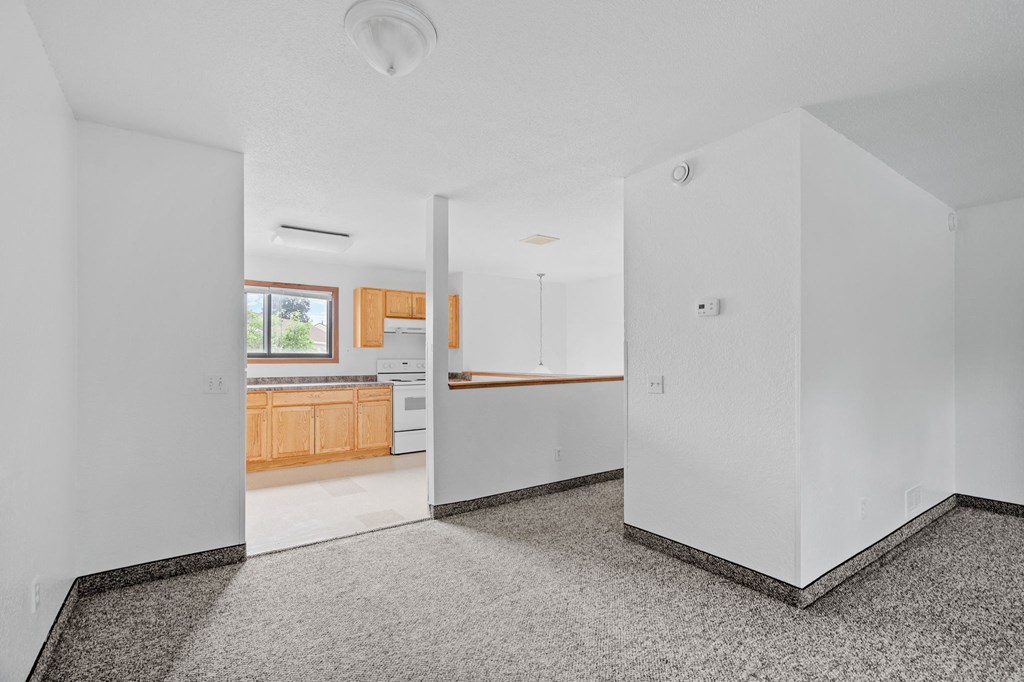 the living room and kitchen of a home with white walls and wood cabinets