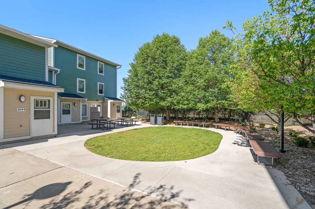 a circular lawn in front of two buildings with trees and a sidewalk