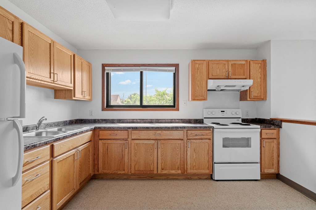 a kitchen with wooden cabinets and white appliances and a window