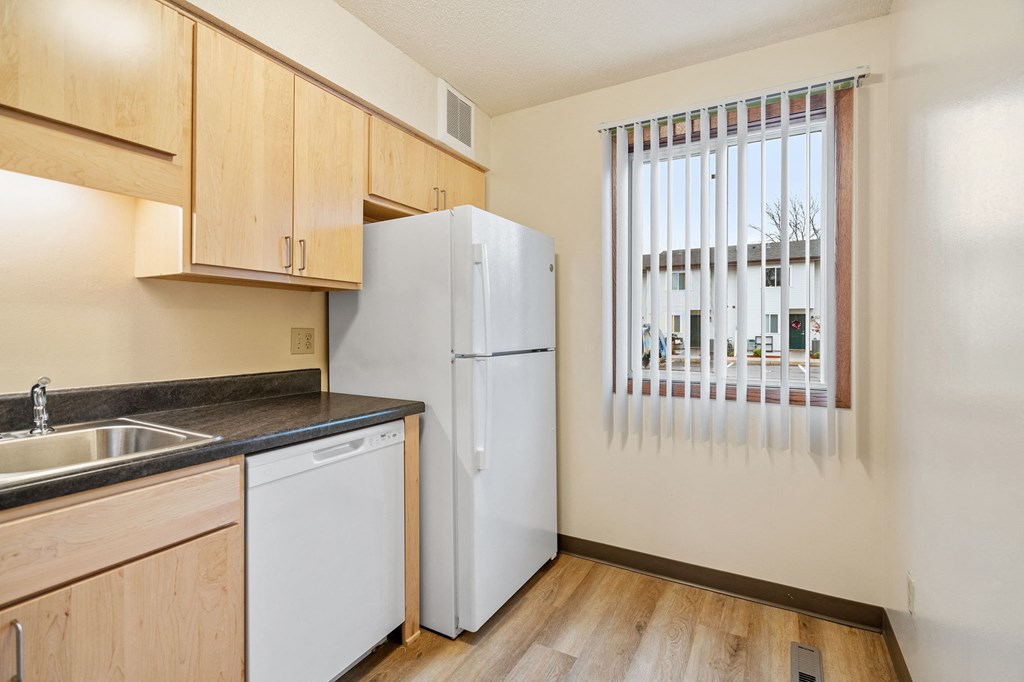 A kitchen with a white refrigerator, wooden cabinets, and a window with blinds.