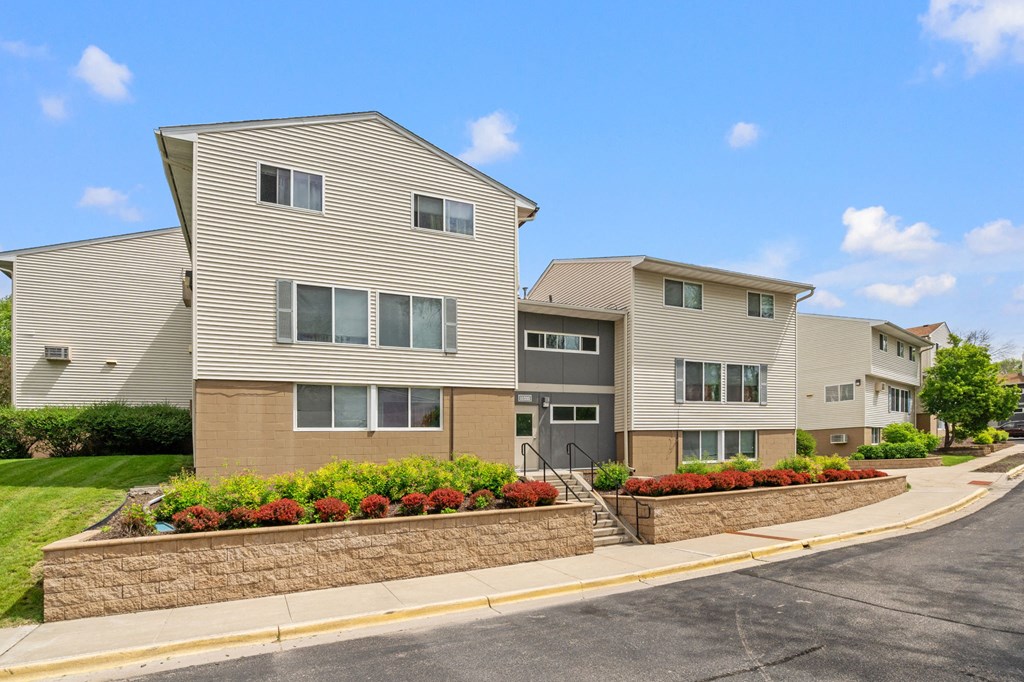 an apartment building with a stone retaining wall and flower beds