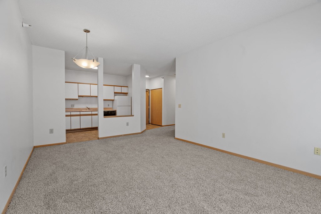 the living room and kitchen of an empty house with white walls and carpet