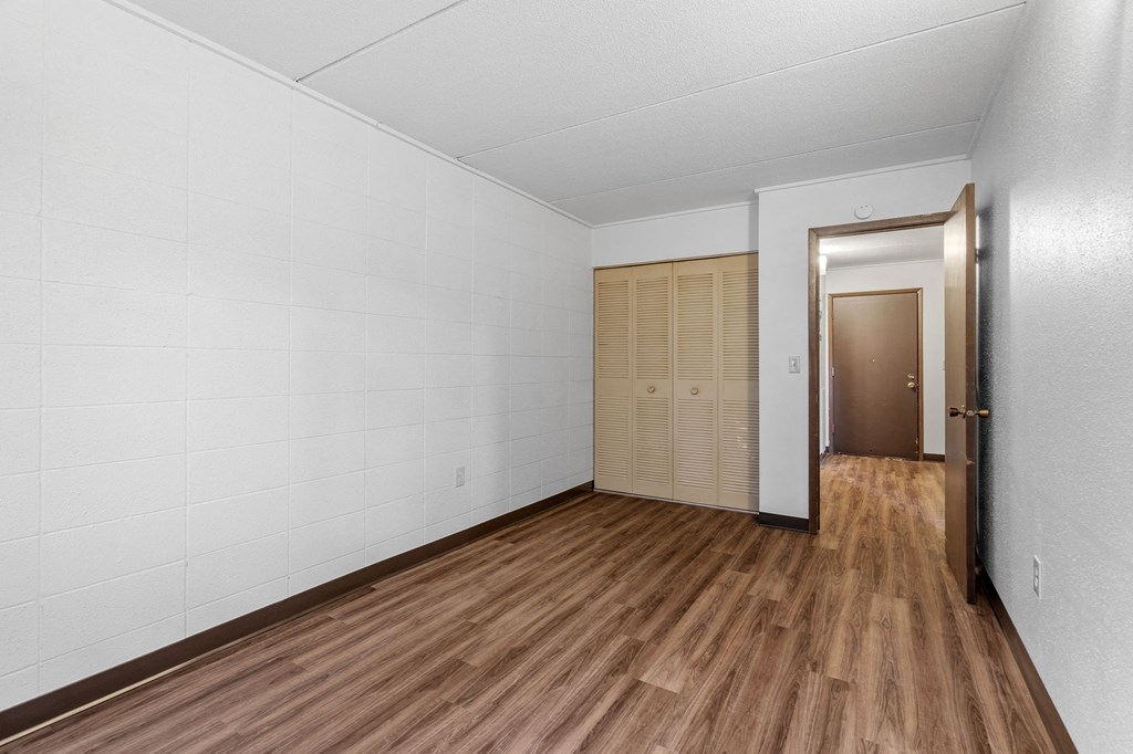 an empty living room with white walls and wooden floors and a closet