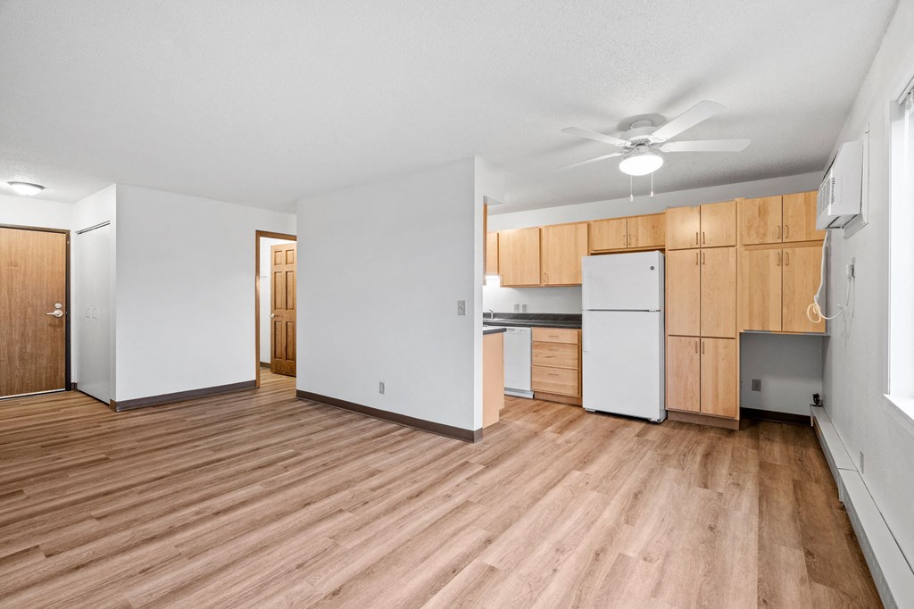 an empty living room and kitchen with wood floors and white walls