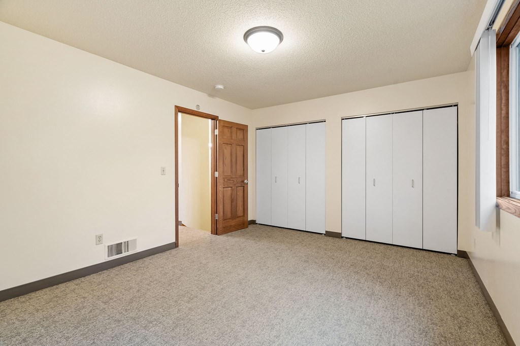 A room with a carpeted floor, a ceiling light, and a door leading to another room.