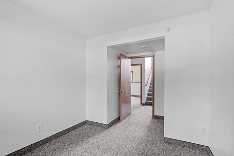 a bedroom with white walls and a door to a hallway with stairs