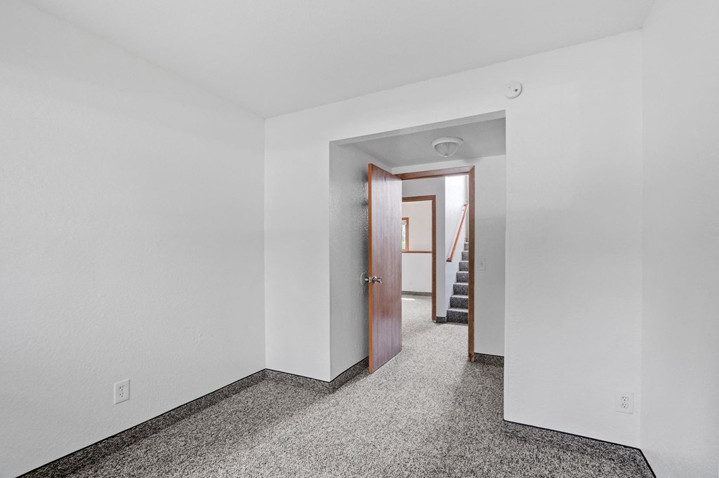 a bedroom with white walls and a door to a hallway with stairs