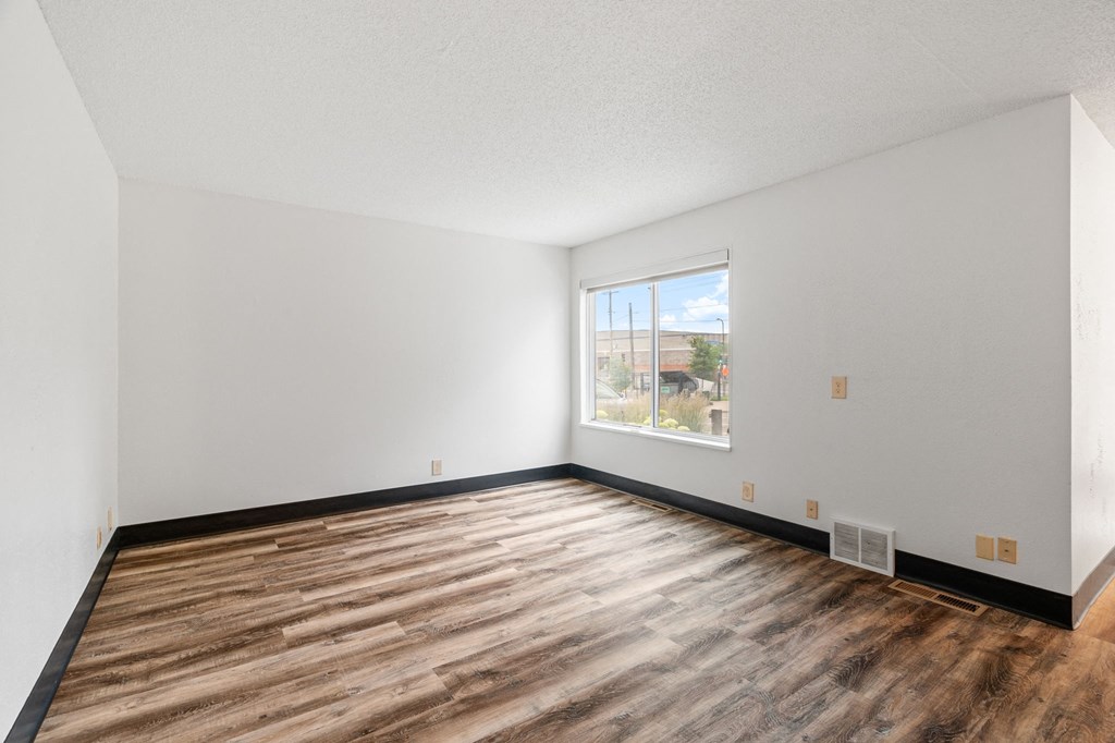 the living room of an apartment with wood flooring and a window