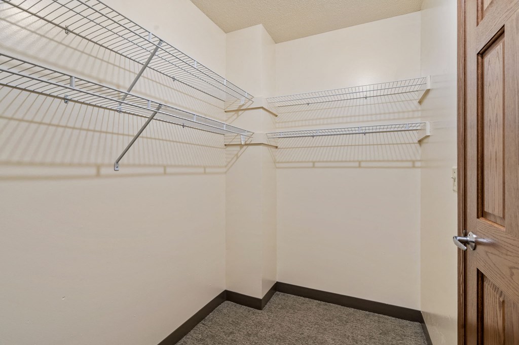 A walk-in closet with white shelves and a brown door.