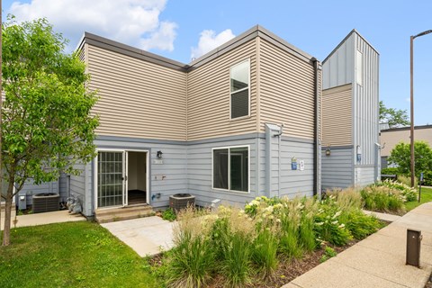 the front of a gray house with a sidewalk and grass