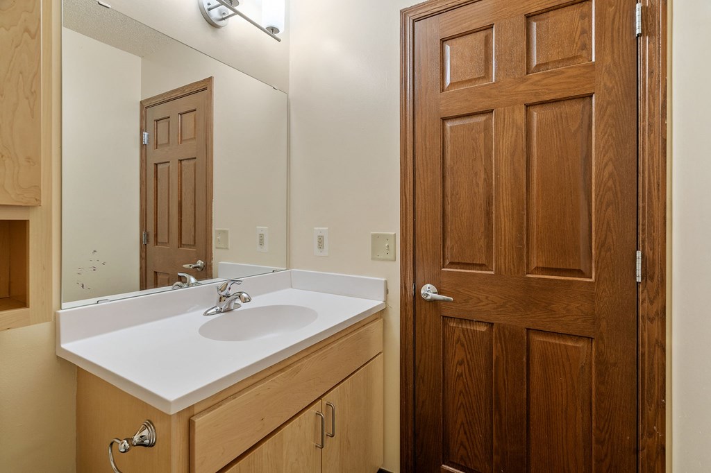 A bathroom with a sink, mirror, and wooden door.