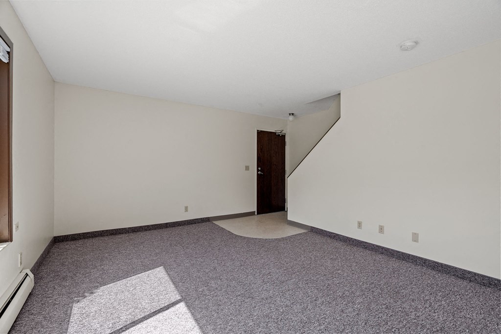 an empty living room with carpet and a door to a staircase