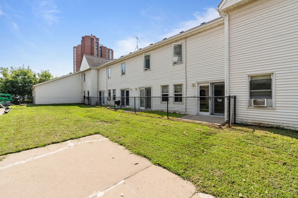 the back of a white house with a yard and a chain link fence