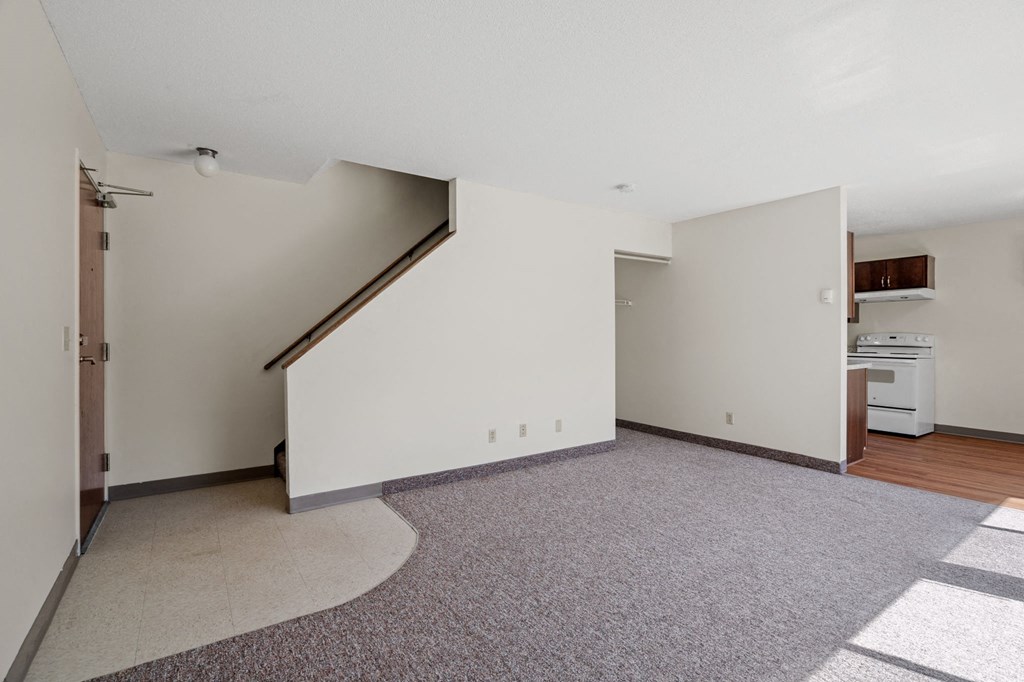 an empty living room with white walls and a kitchen with a stove and a door
