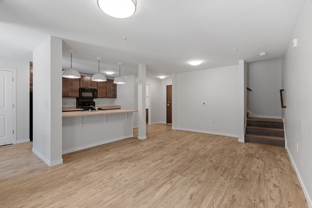 an empty living room with a kitchen and stairs