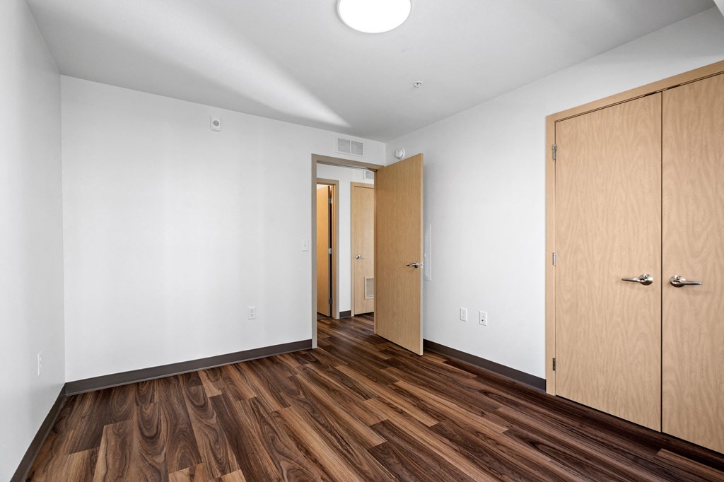 a bedroom with white walls and wood flooring and a closet
