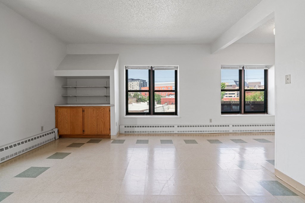 an empty living room with three windows and a tile floor