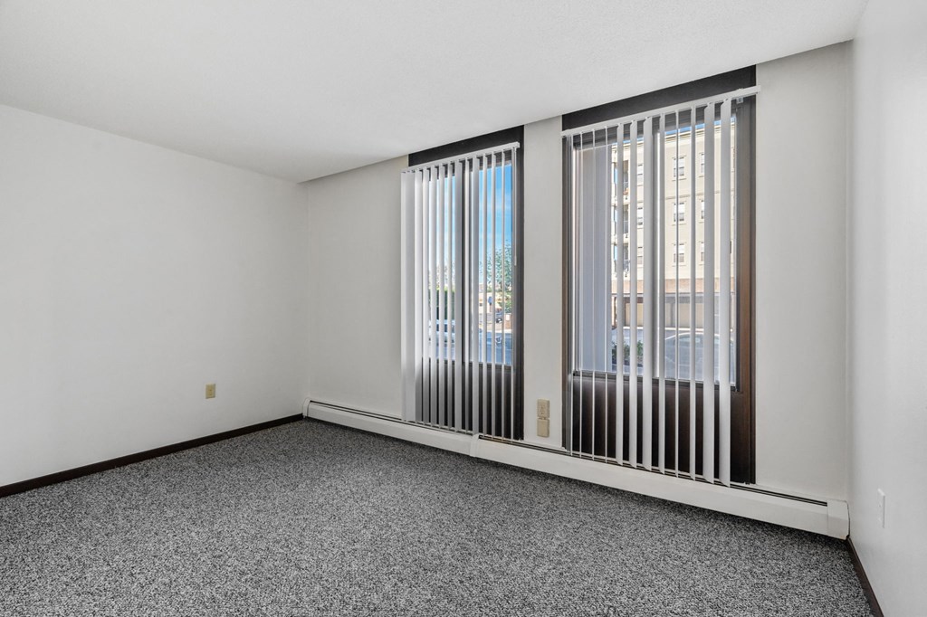 an empty living room with large windows and gray carpet