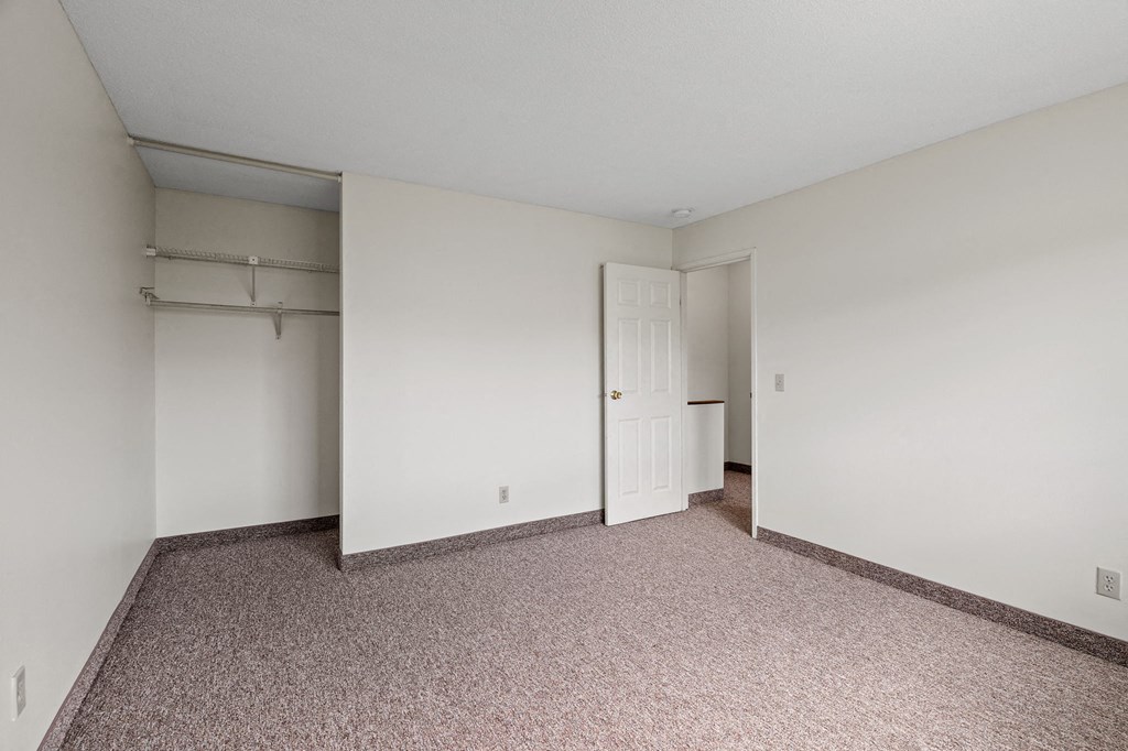 a bedroom with white walls and carpet and a door to a closet