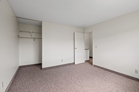 a bedroom with white walls and carpet and a door to a closet