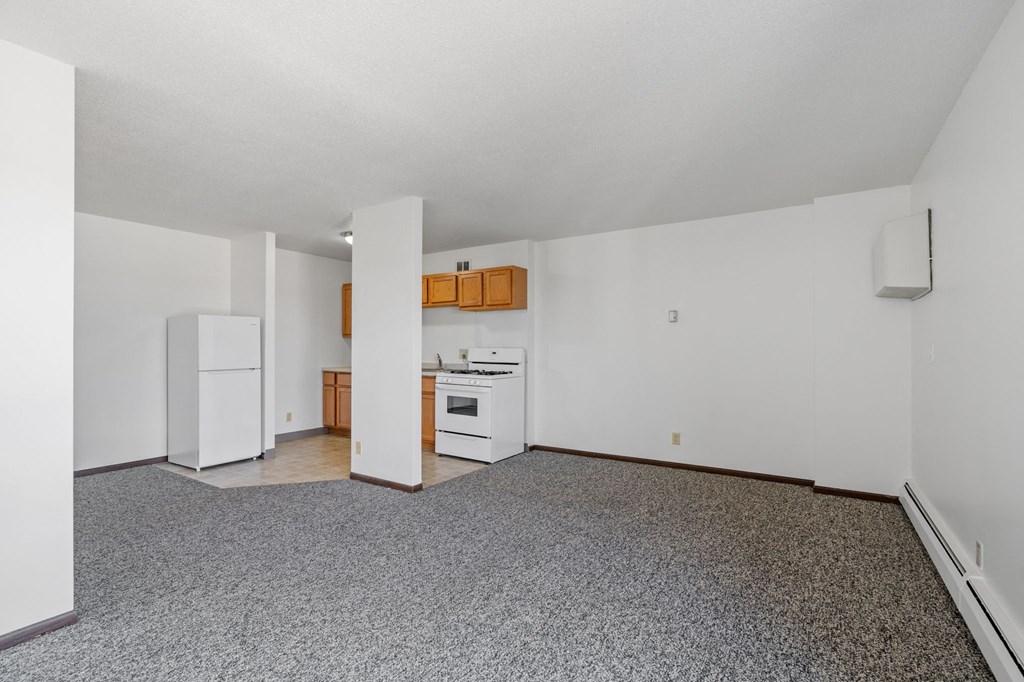 an empty living room with a kitchen with a stove and refrigerator