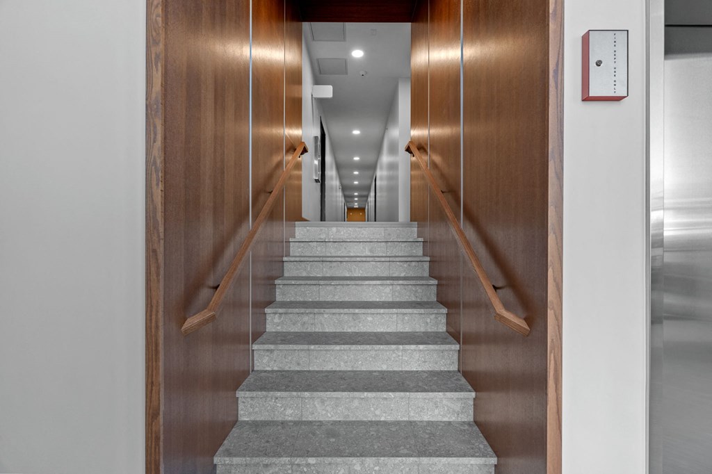 a staircase with grey carpeting leading up to a hallway with wooden doors
