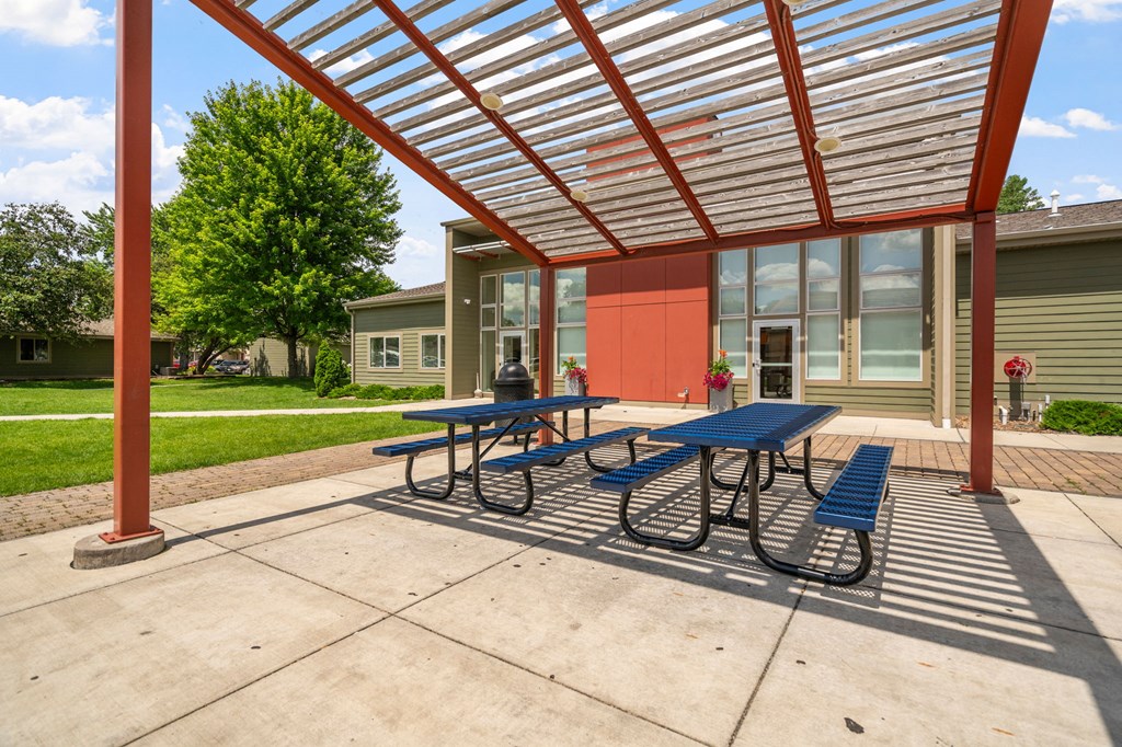 a covered picnic area with benches and tables in front of a building