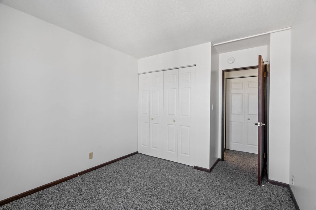a bedroom with white walls and carpet and a door to a closet