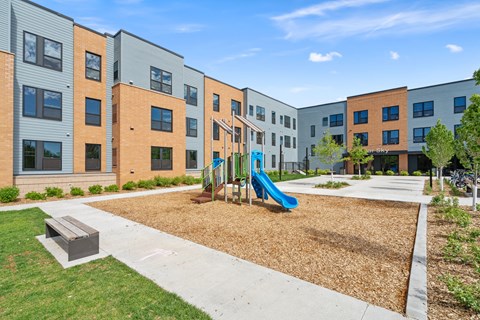 A playground area with a slide and a bench in front of apartment buildings.