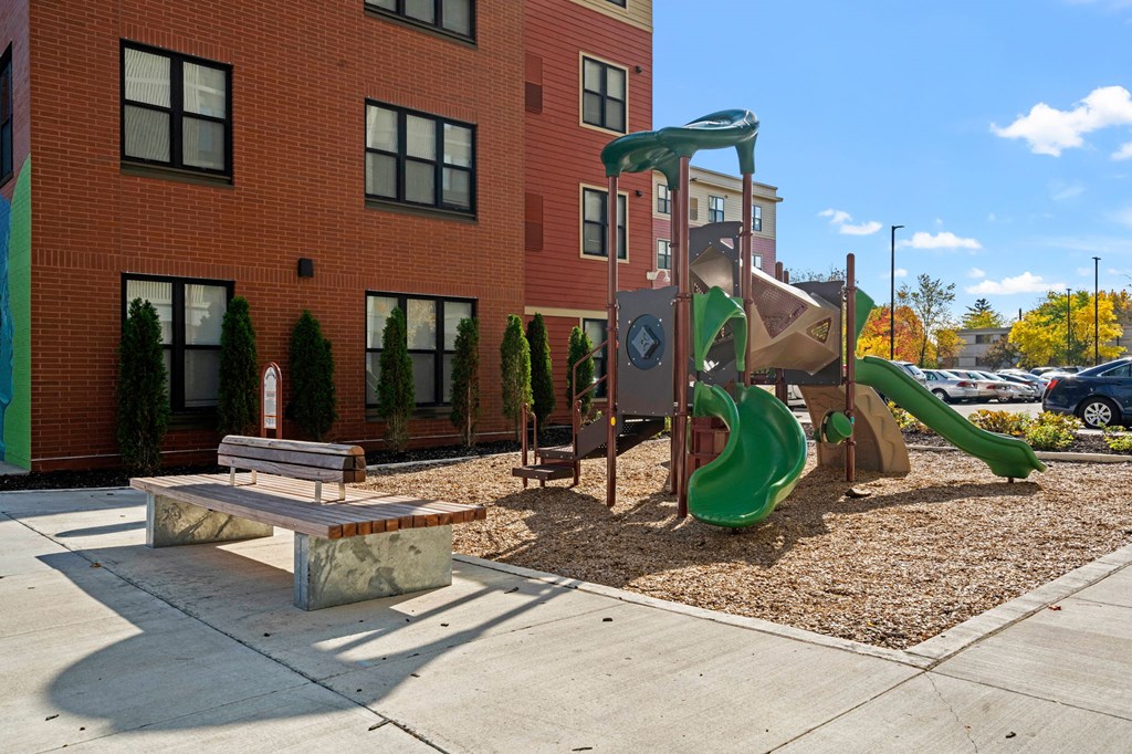 a playground with a slide and a bench in front of a building