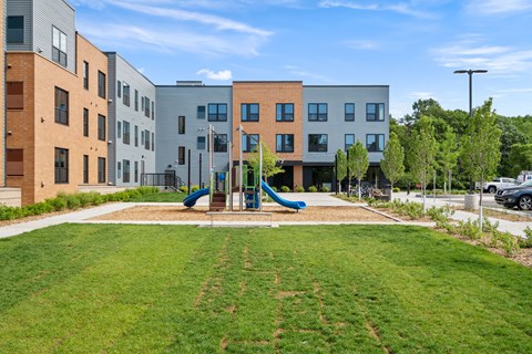 A playground with a slide is in front of apartment buildings.