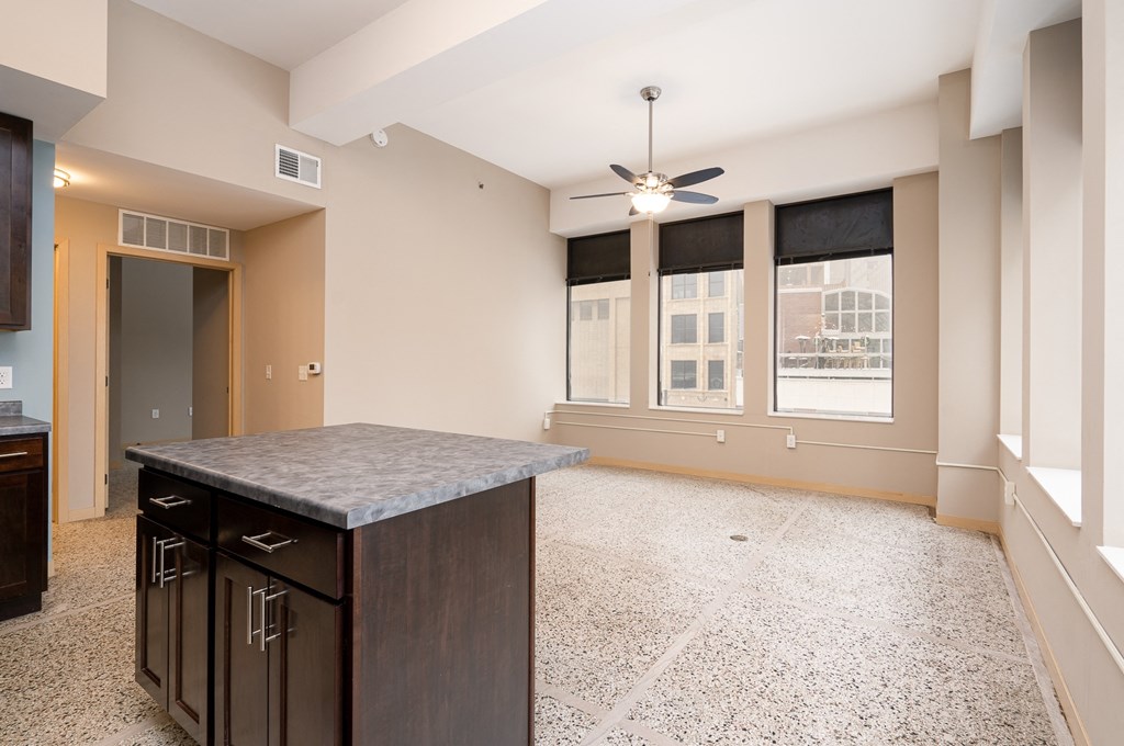 an empty living room with a kitchen island and a ceiling fan