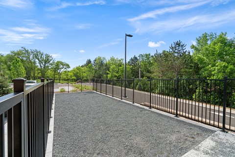 A gravel parking lot with a metal fence and trees in the background.