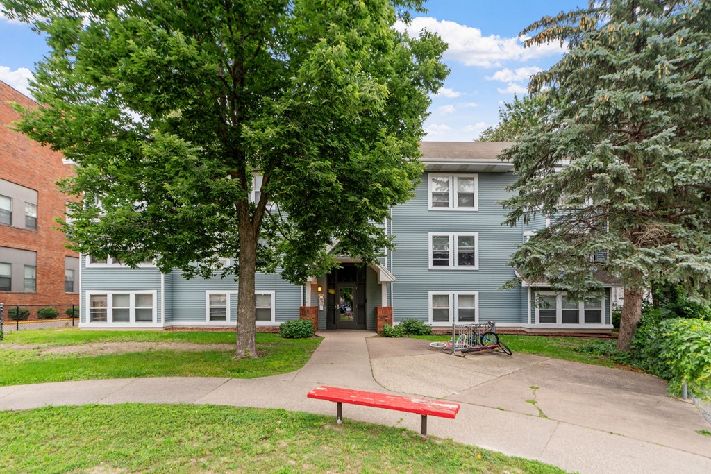 a red bench sits in front of a blue building with trees