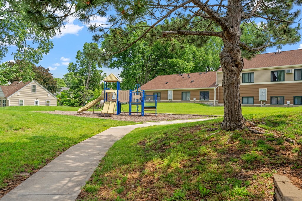 a sidewalk leading to a playground with a blue swing set