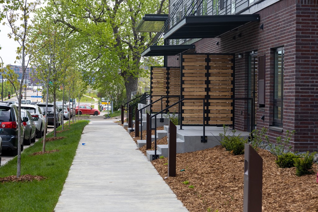 a sidewalk in front of a building with trees and cars parked