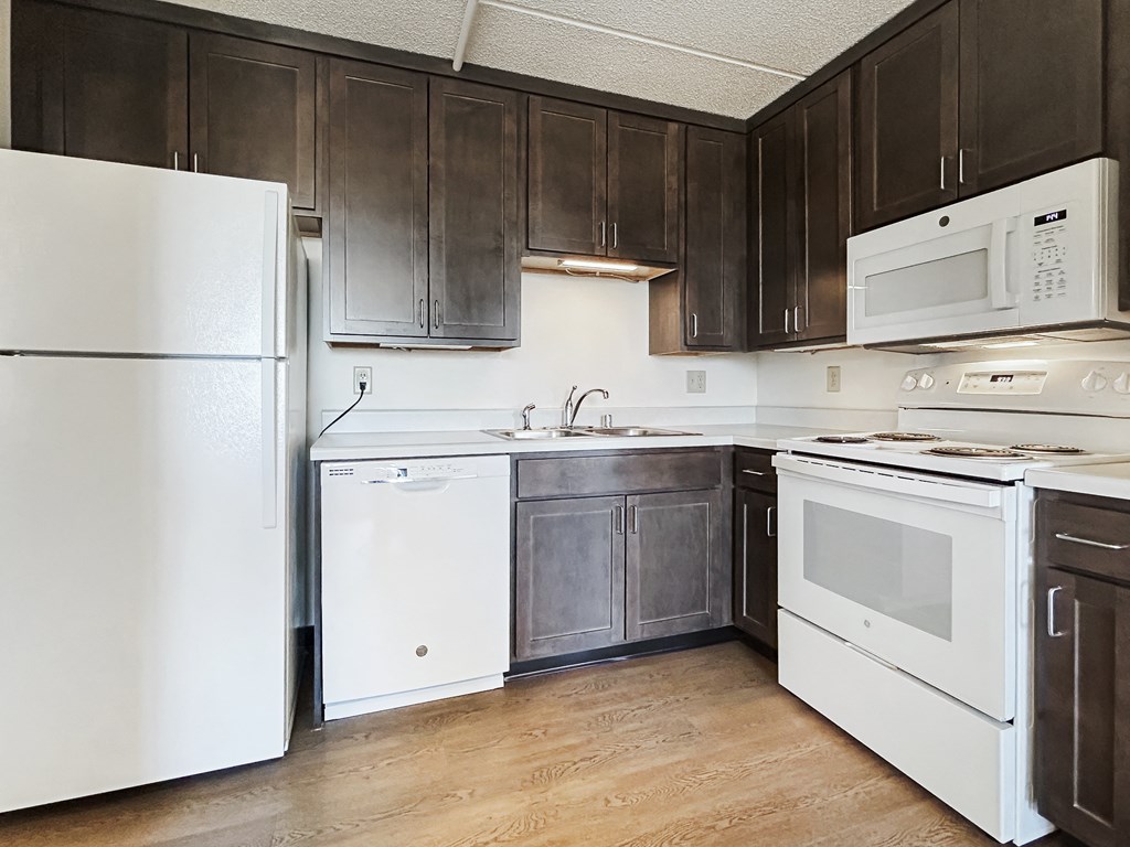 an empty kitchen with white appliances and dark cabinets