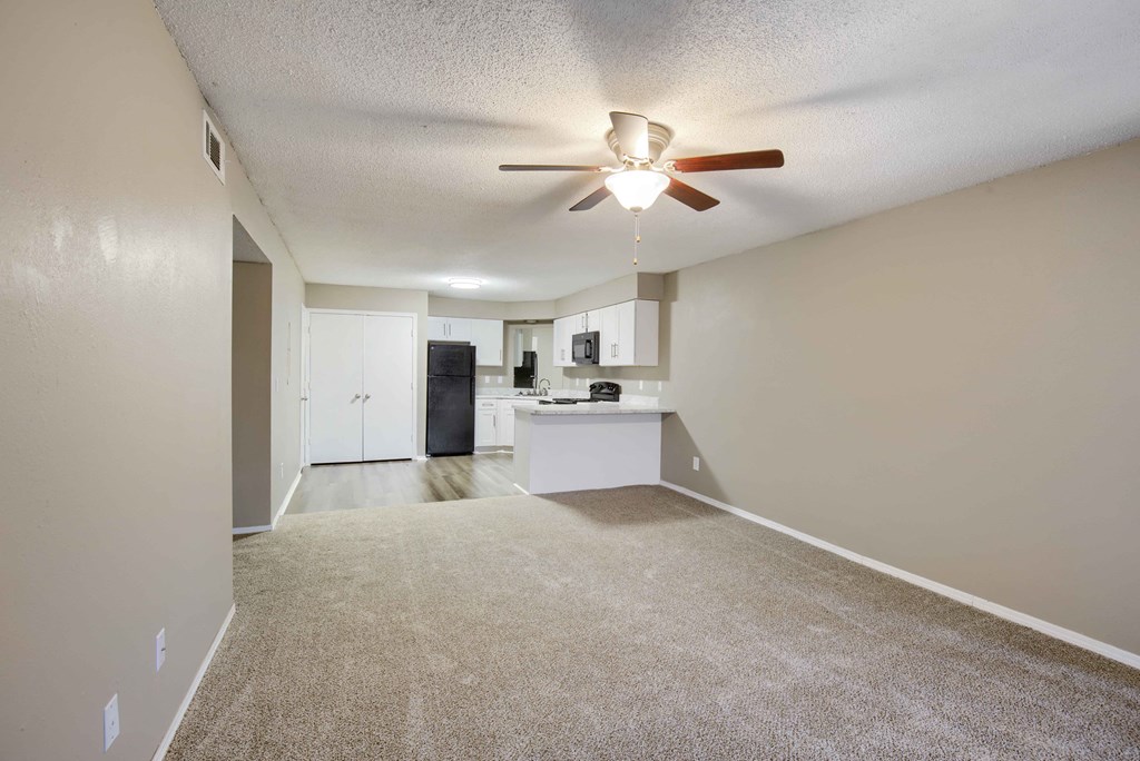 a living room with a ceiling fan and a kitchen in the background