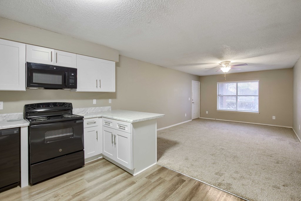 a kitchen and living room with white cabinets and a black stove top oven